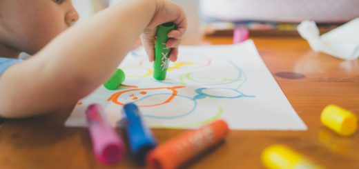 Dítě kreslí u stolu s voskovkami – ilustrační fotografie
